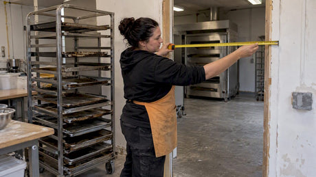 Bakery owner checking doorway clearance beside trays